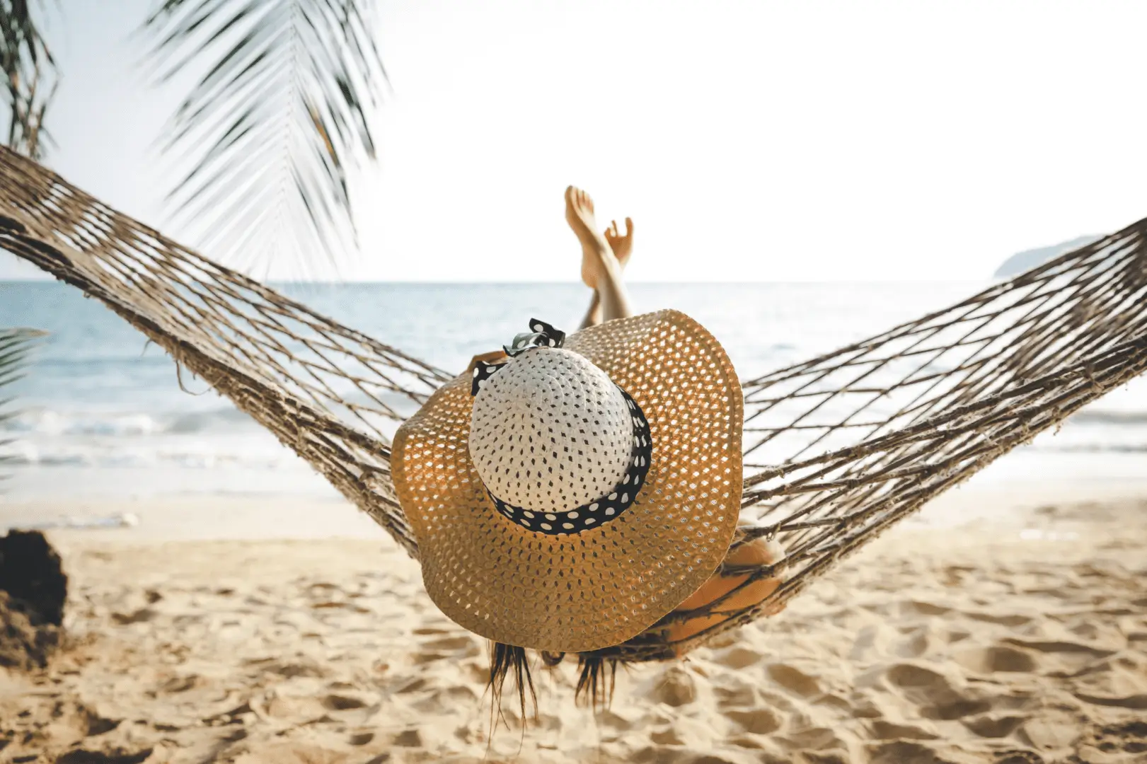 Person in straw hat relaxing in beach hammock